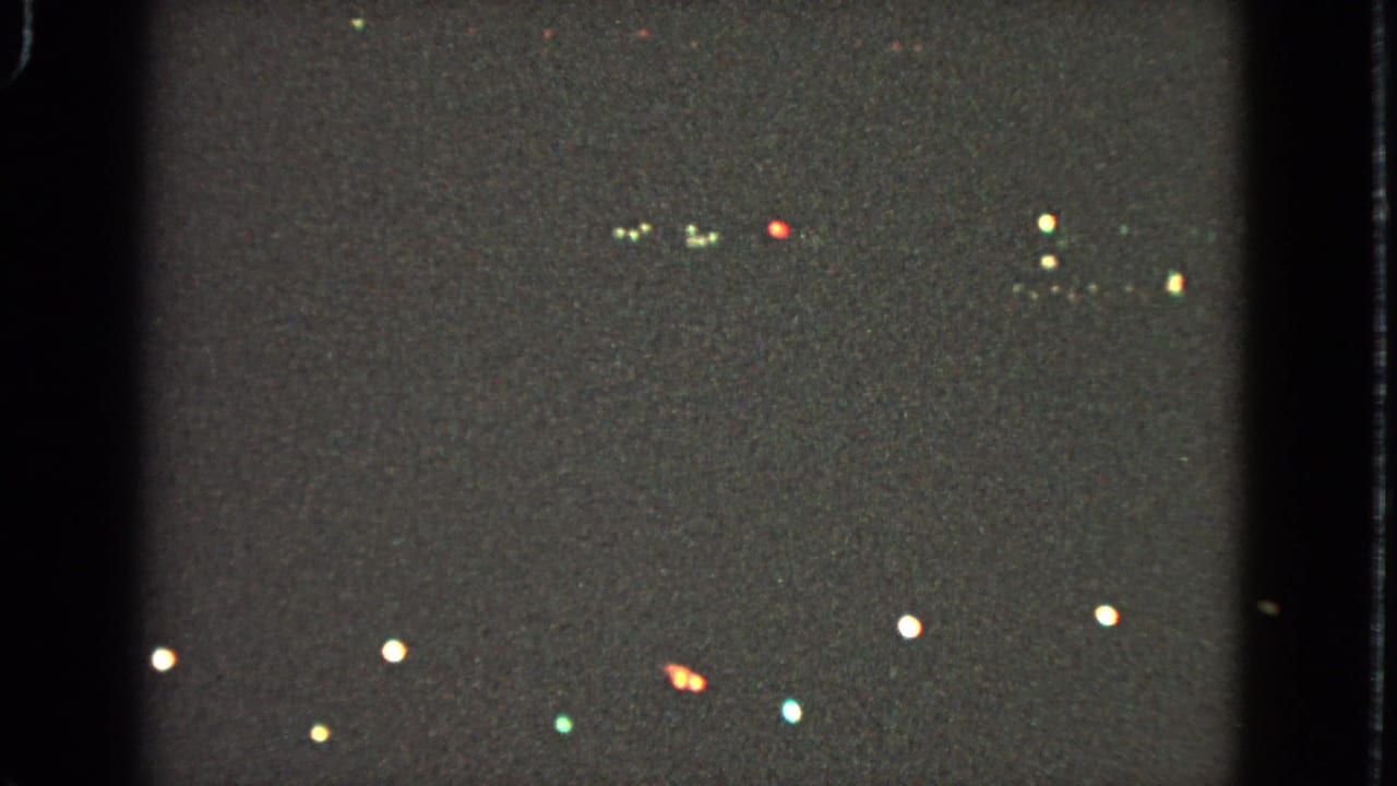 1963 Barrington home-movie frame showing scattered Christmas lights as soft colored points against a dark night scene.