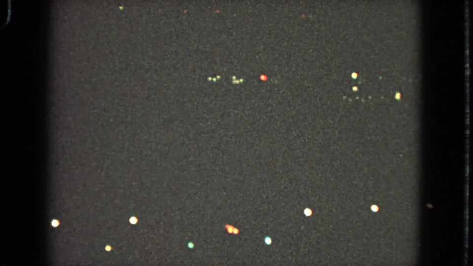 1963 Barrington home-movie frame showing scattered Christmas lights as soft colored points against a dark night scene.
