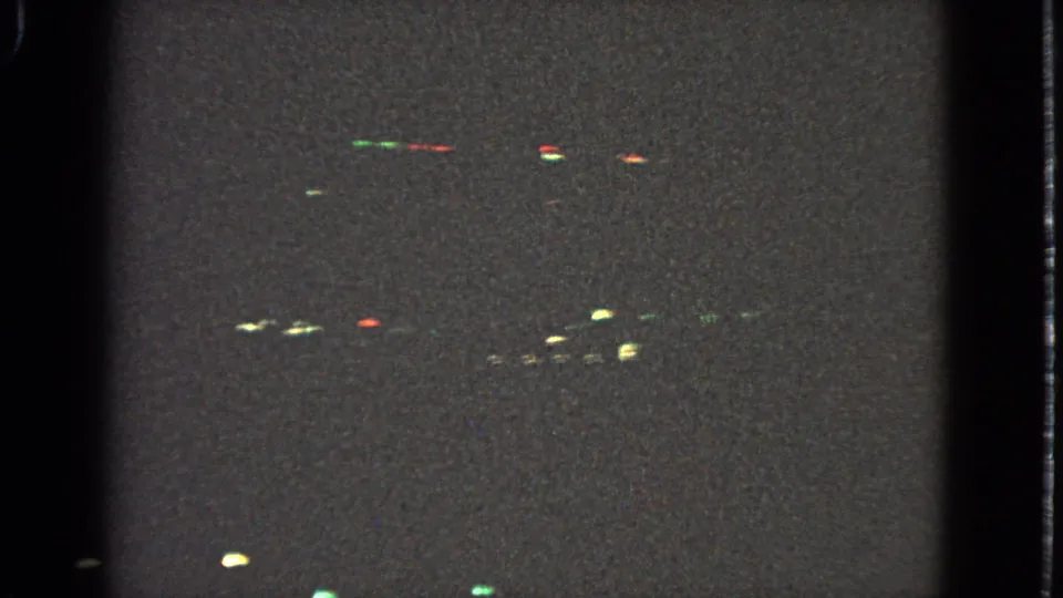 Barrington 1963 nighttime drive frame with clustered Christmas lights rendered as soft colored bokeh on 8mm film.
