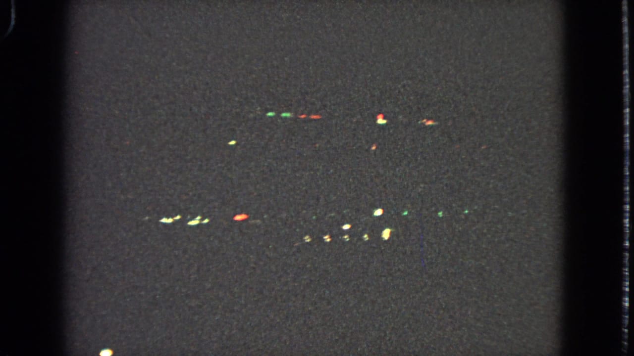 Dark airplane-window view with scattered colored lights in the distance.