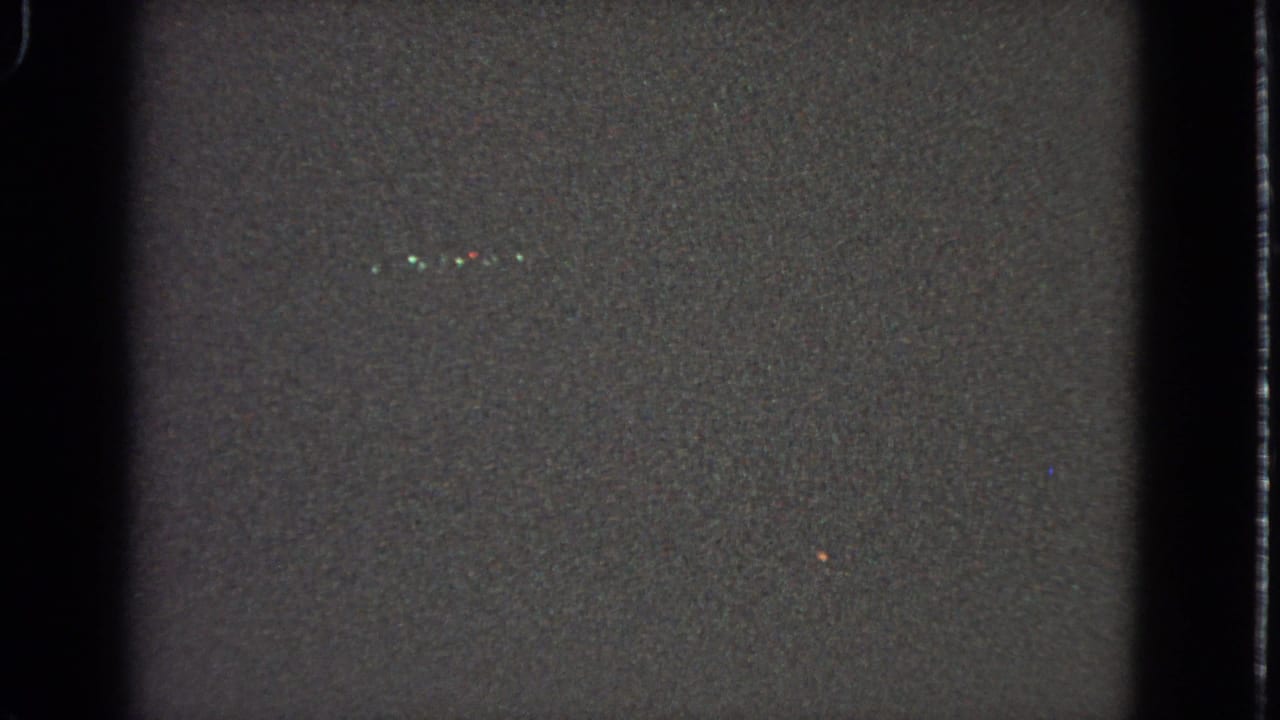 Dark grainy 8mm frame with vertical film borders and a few small light specks.