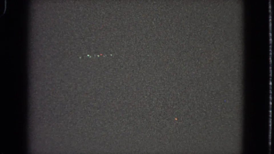 Dark opening frame from an 8mm scan, showing film grain, vertical borders, and scattered light specks before the street sign appears.