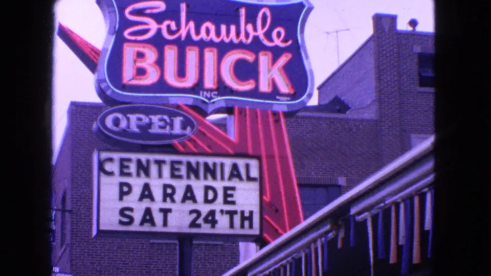 Steady 8mm view of Schauble Buick and Opel signage with a Centennial Parade Sat 24th marquee in Barrington, Illinois.