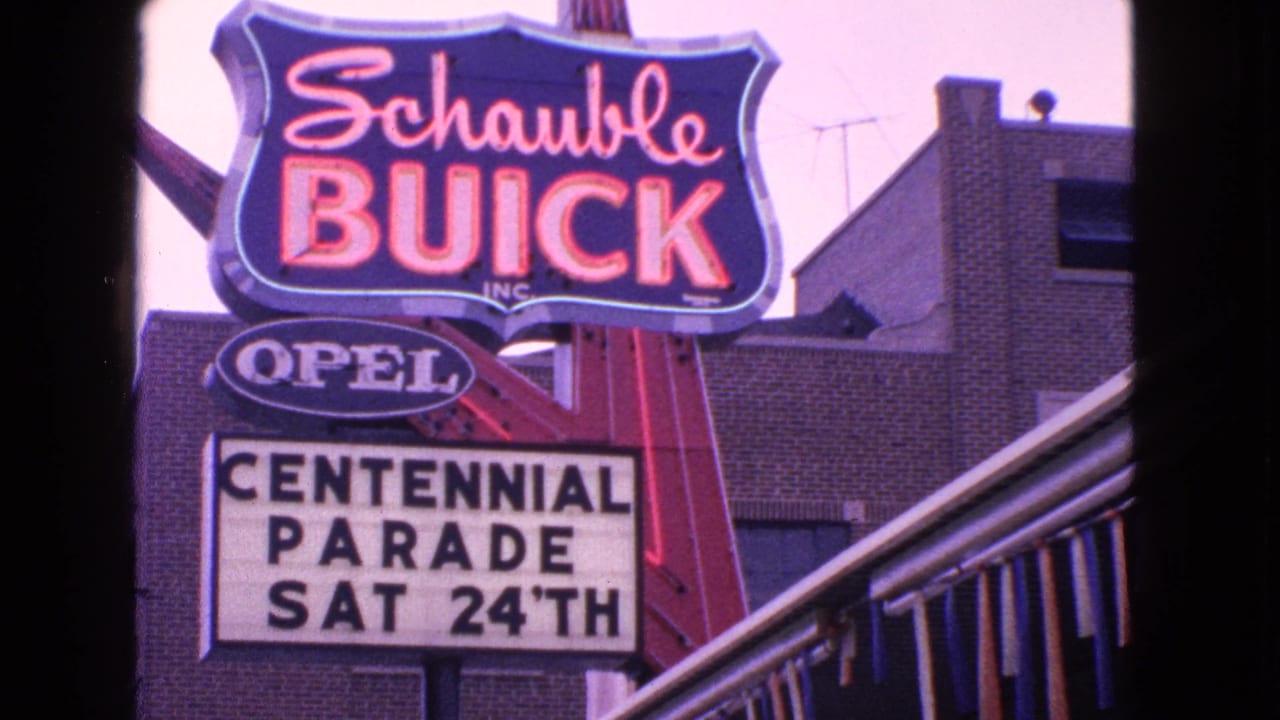 Schaubie Buick and Opel signs above a marquee reading Centennial Parade Sat 24th.