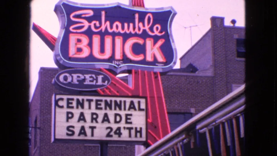 1963 Barrington, Illinois view of the Schaubie Buick dealership sign with Opel branding and the Centennial Parade marquee below.