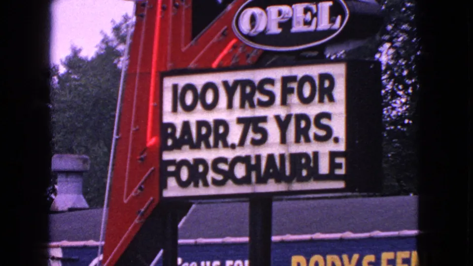 1960s home-movie frame of the Barrington Opel sign, with the marquee text most legible and trees in the background.