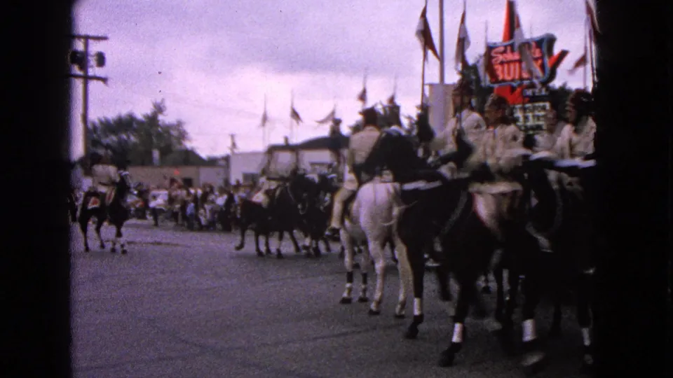 Barrington parade riders in light uniforms and dark hats pass close to the camera on black and white horses.