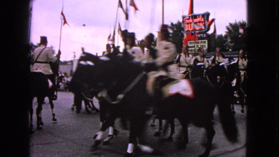 1963 Barrington parade view with uniformed riders passing the camera, flags overhead, and spectators near the Schwab's Buick sign.