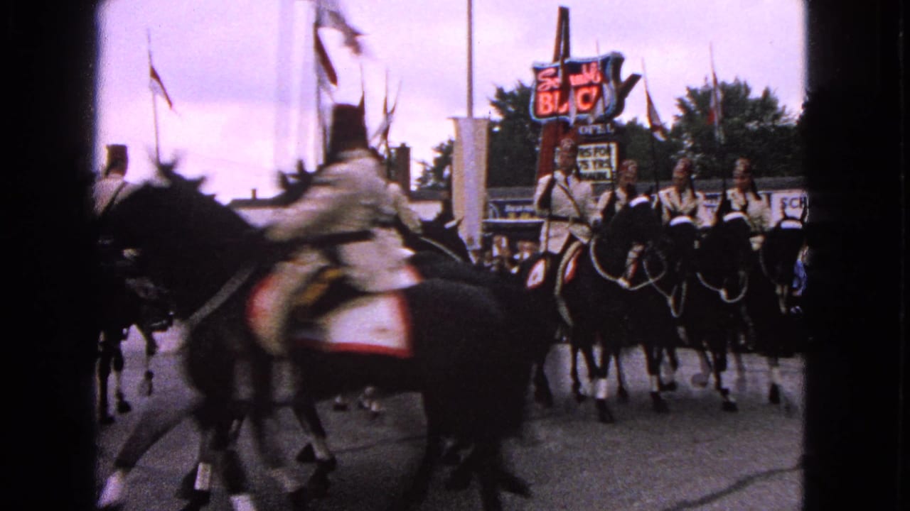1963 Barrington, Illinois parade scene with horseback riders moving past the camera near flags and a Schumacher Buick sign.