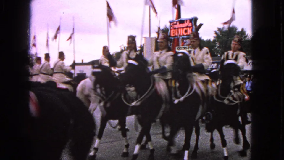 Close parade view of uniformed horseback riders in Barrington, Illinois, with horses, flags, and a Schumacher Buick sign in frame.