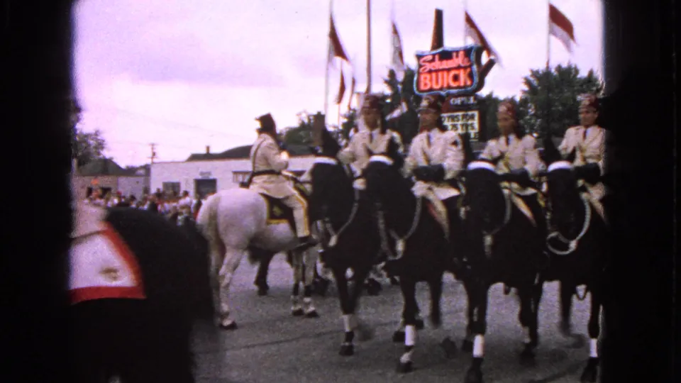 1963 Barrington parade footage showing riders on black and white horses moving along a street near visible flags and Buick signage.