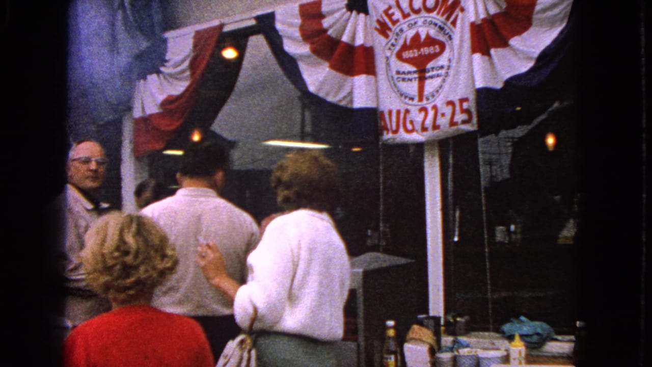 Barrington, Illinois centennial storefront scene with adults gathered below red, white, and blue bunting in 1963 home-movie footage.