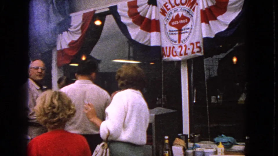 Barrington, Illinois centennial storefront scene with adults gathered below red, white, and blue bunting in 1963 home-movie footage.