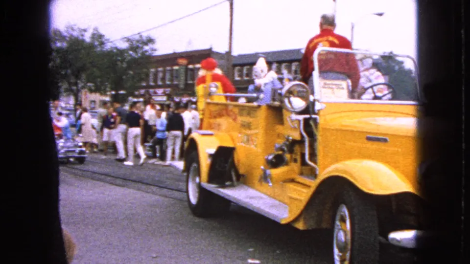 Yellow fire truck float with costumed clowns passes a sidewalk crowd during the 1963 Barrington Centennial parade.