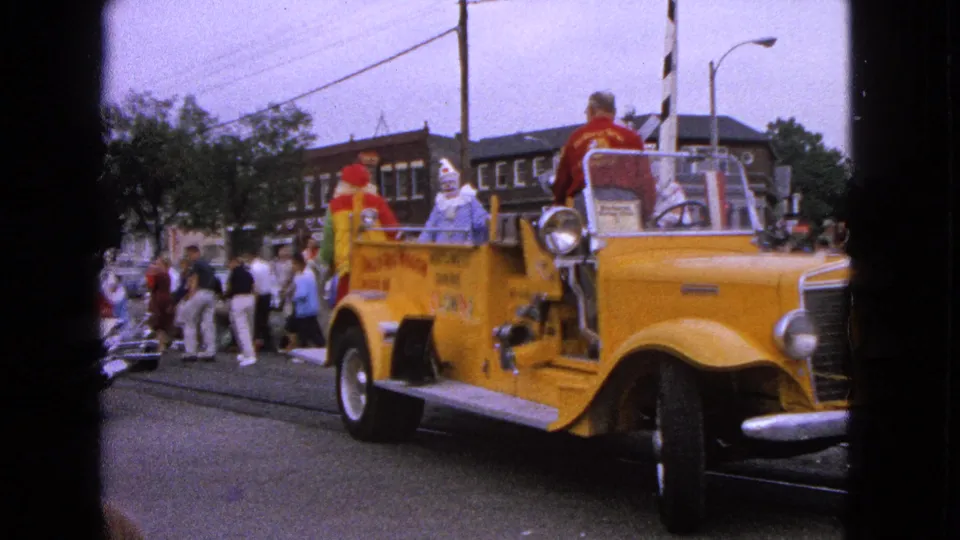 Closer view of the yellow fire truck float and clowns passing spectators in Barrington, Illinois, in 1963.