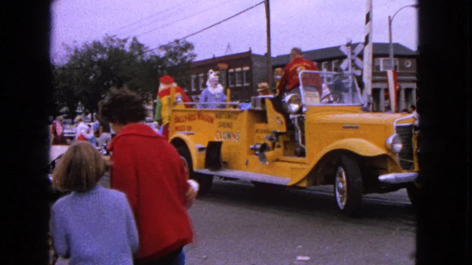 Curbside spectators, including a woman in red, watch the yellow clown fire truck float in the Barrington Centennial parade.