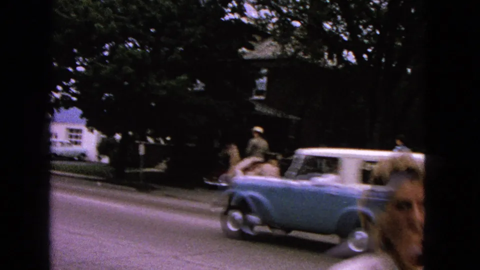 A mid-century blue-and-white car crosses the Barrington street scene as a mounted or wagon participant remains partly visible.