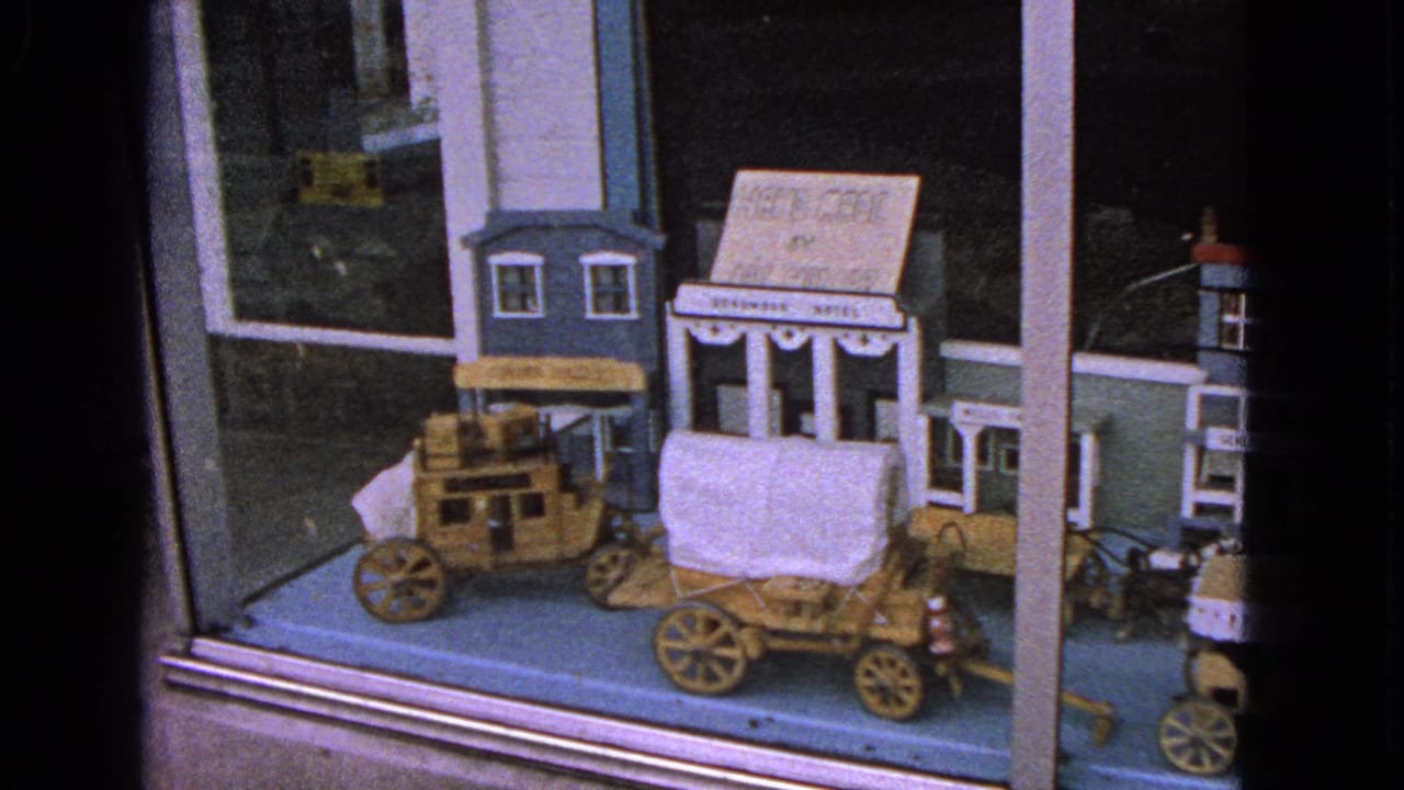 1963 Barrington, Illinois home-movie frame showing a wooden Western town display with a covered wagon and storefronts behind glass.