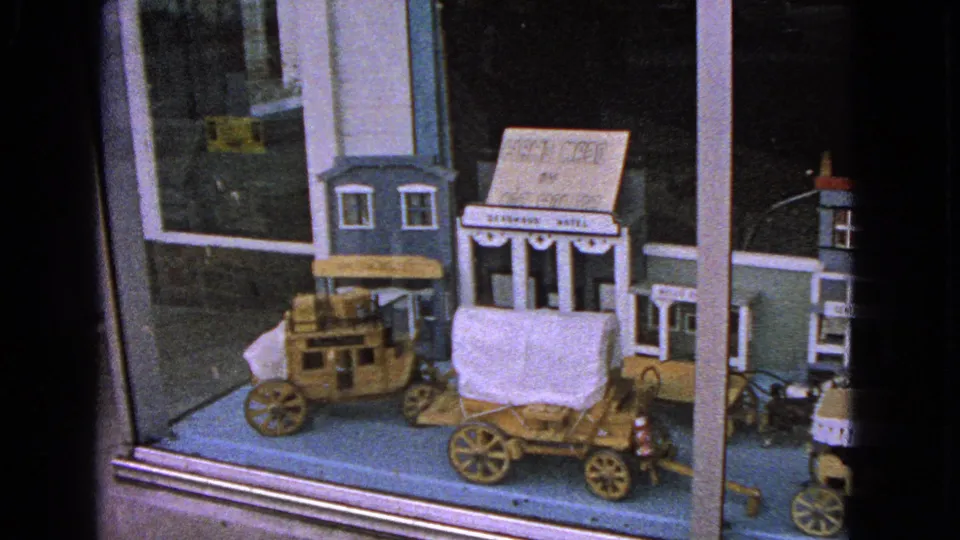 Wooden Western-themed toy wagons and storefront models appear in a Barrington shop-window display, filmed on 8mm in 1963.
