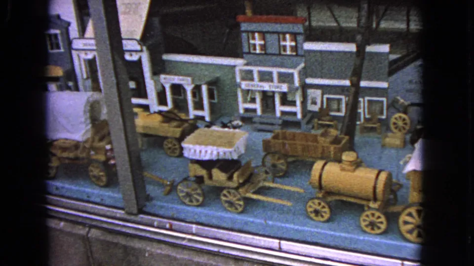 The final frame shows the 1963 Barrington wooden Western toy town display with storefronts, wagons, barrels, and visible window reflections.