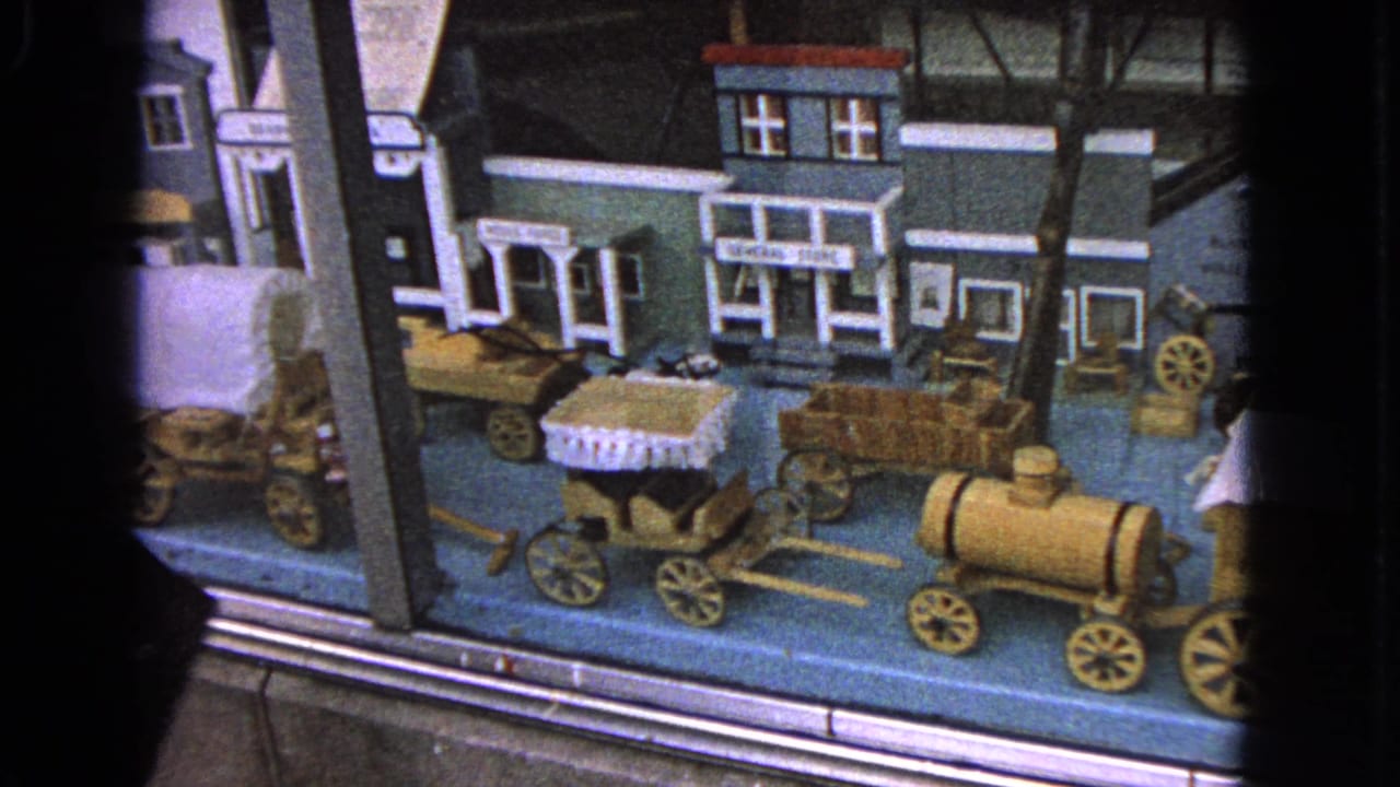 Miniature town display with wagons, storefronts, and a small train engine behind glass.