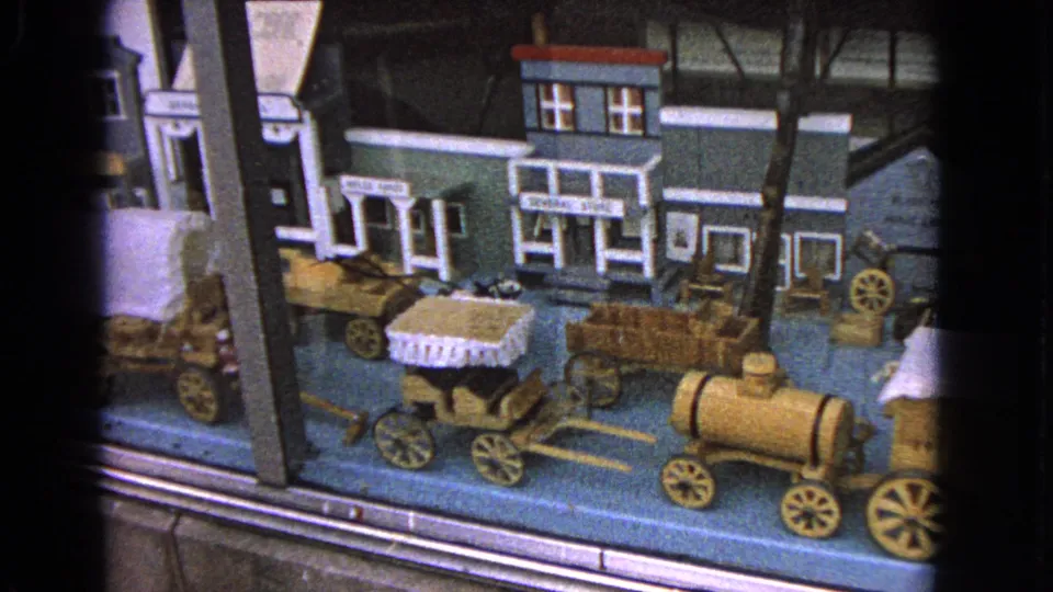 The frame shows a Barrington model town display with small shop facades, wooden wagons, and a train-like engine on a blue base.