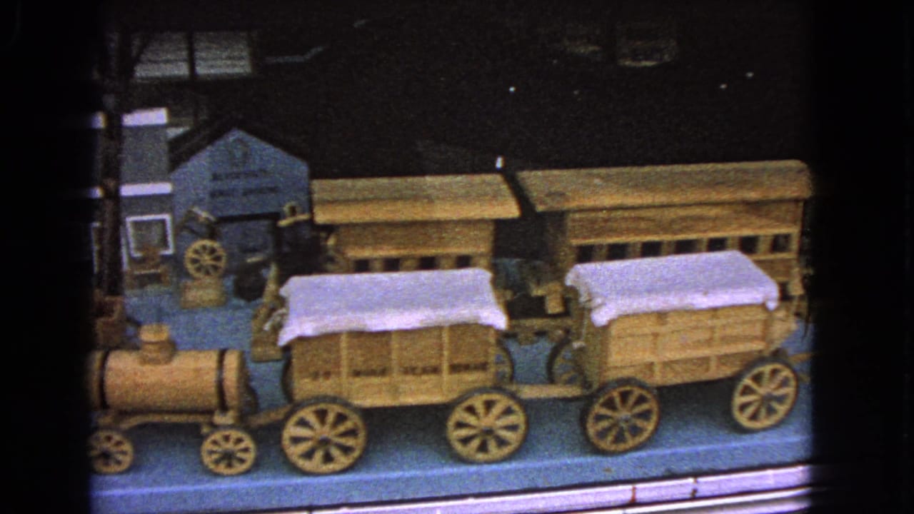 Wooden toy train and covered wagons displayed behind glass.