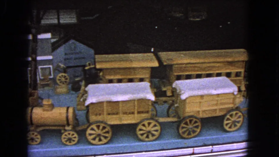 1963 Barrington, Illinois 8mm frame showing a wooden toy train with covered wagons inside a glass display case.