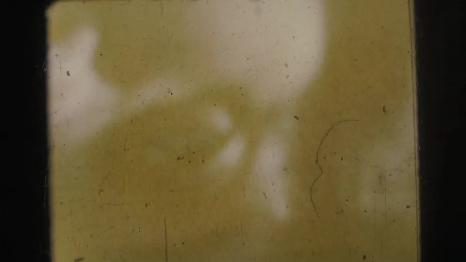 Faded 8mm frame from the 1963 Bowling Green University reel showing abstract yellow-green exposure, scratches, dust, and dark film borders.