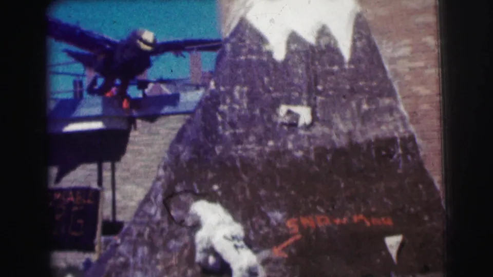 The final frame shows a display or diorama with a dark bird figure, painted mountain-like backdrop, snowman figure, and partial signage on faded 8mm film.