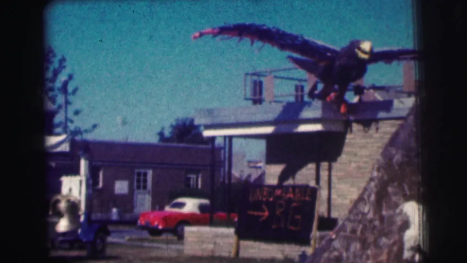1963 Bowling Green University footage shows the fake eagle prop above buildings, a red car, chalkboard sign, and a person at lower left.