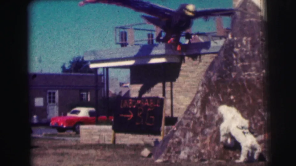 1963 Bowling Green University frame with the fake eagle prop over a building, red car below, and hand-lettered sign in the foreground.