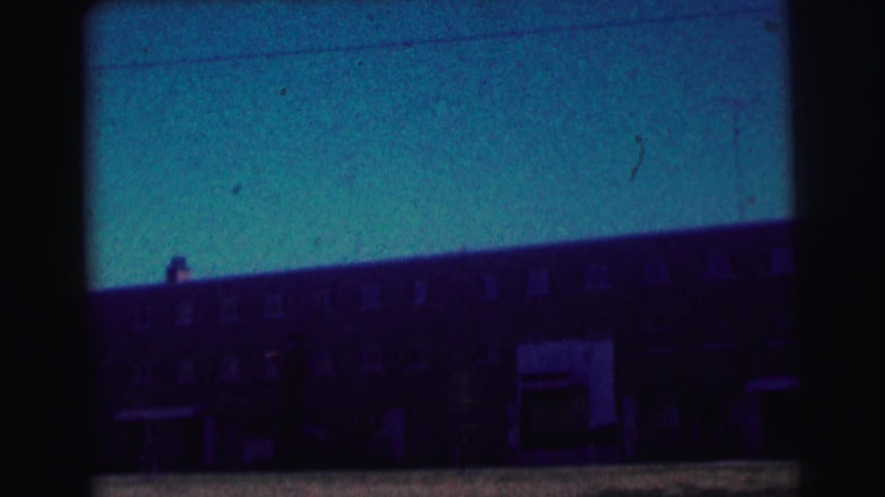 Dark long brick building under a blue sky, with windows and a central entrance area.