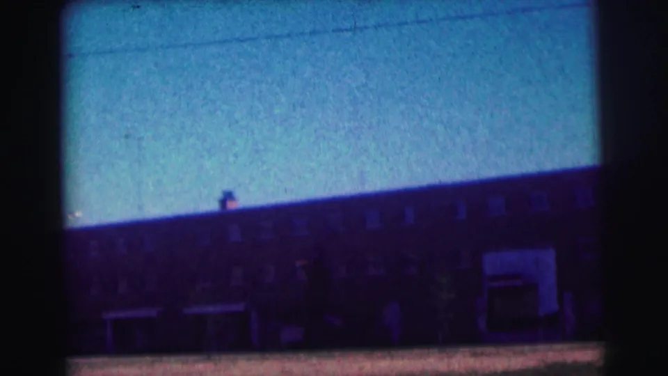 Final 8mm frame of the Bowling Green University exterior, showing a long brick facade, small windows, and open foreground under a blue sky.