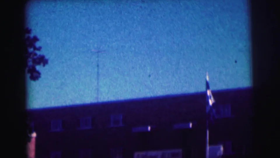 Bowling Green University exterior with flagpole, roofline, and blue sky in a grainy 1963 8mm home-movie frame.