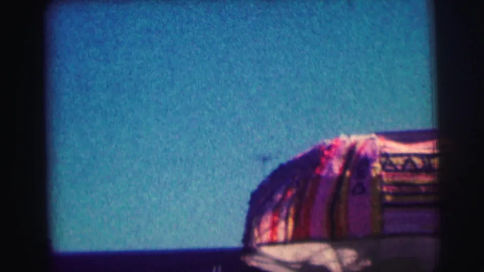 Later frame shows a colorful striped textile or structure in the foreground beneath blue sky, partly obscured by 8mm gate shadow.