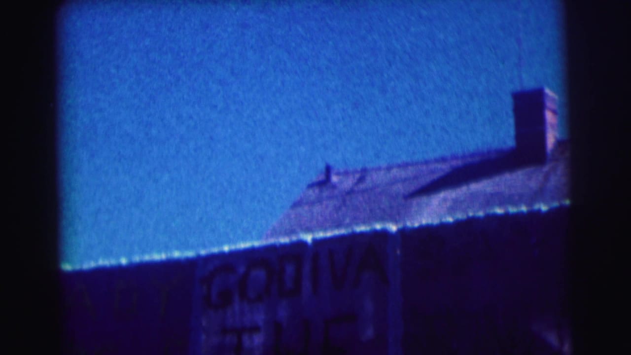 Roofline and chimney above a partially visible Godiva sign under a blue sky.