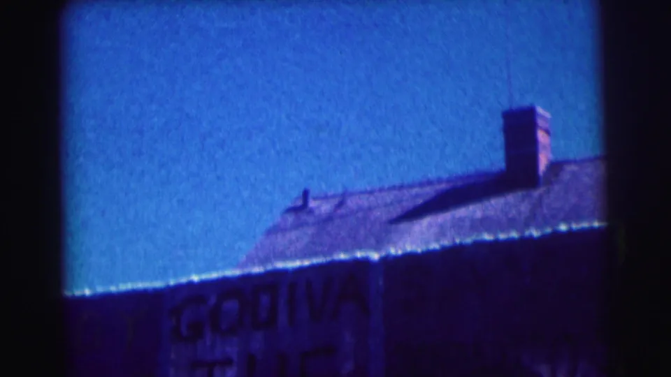 1963 8mm frame at Bowling Green University with cropped Godiva lettering below a sloped roof and chimney in sunlight.