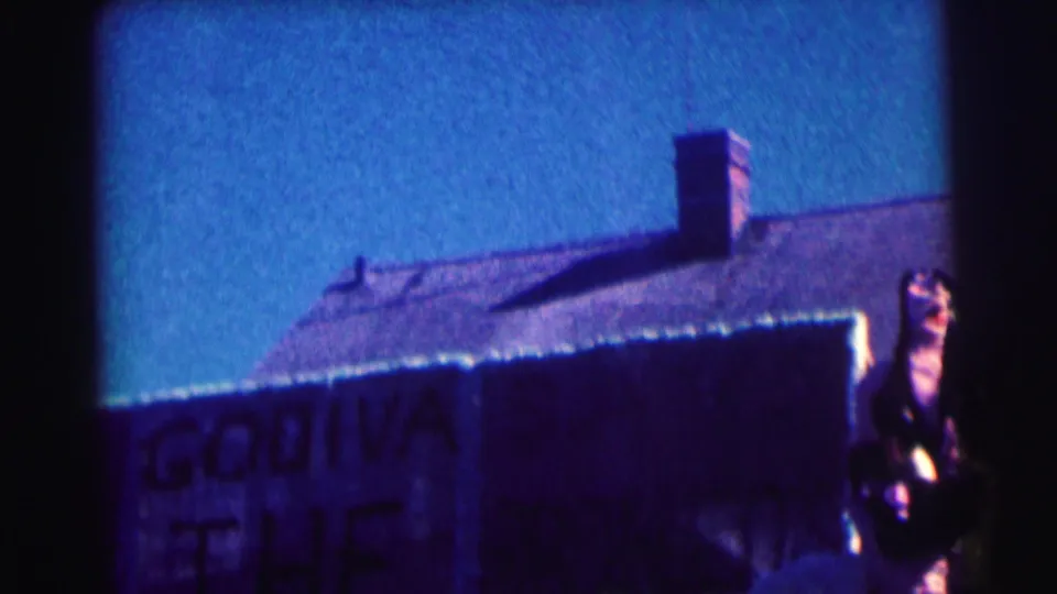1963 8mm frame at Bowling Green University showing the Godiva sign, roofline, chimney, and a partial person at frame right.