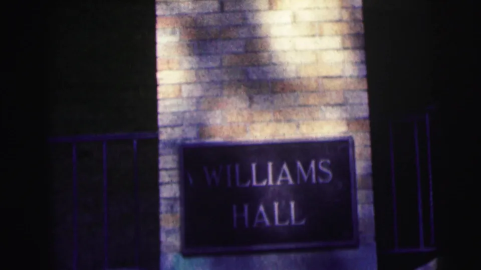 Close 1963 campus frame showing the Williams Hall plaque on brickwork, with strong shadow and saturated 8mm color.