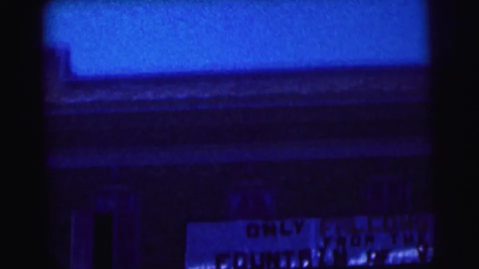 End frame with blue color shift, showing part of the Bowling Green State University sign below a building edge and dark film borders.