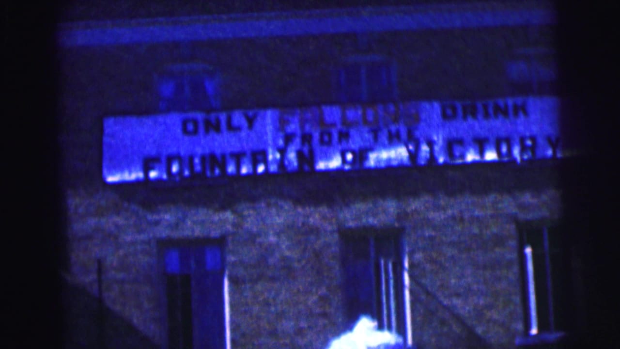 1963 Bowling Green University home-movie frame showing a dark brick building facade and partially readable campus sign.