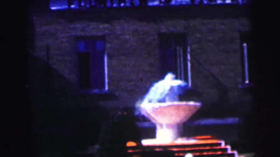 1960s campus home-movie view of a glowing fountain below dark windows at Bowling Green University.