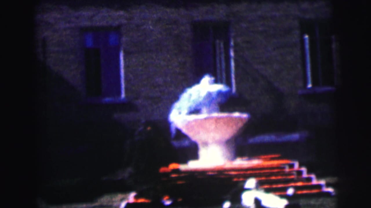 Night view of a lit fountain in front of a dark brick building.