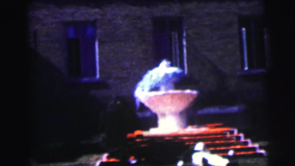 1963 Bowling Green University home-movie frame showing a lit sculptural fountain against a dark brick building facade.
