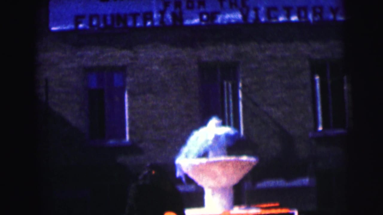 Lit fountain below a building sign with windows in the background.