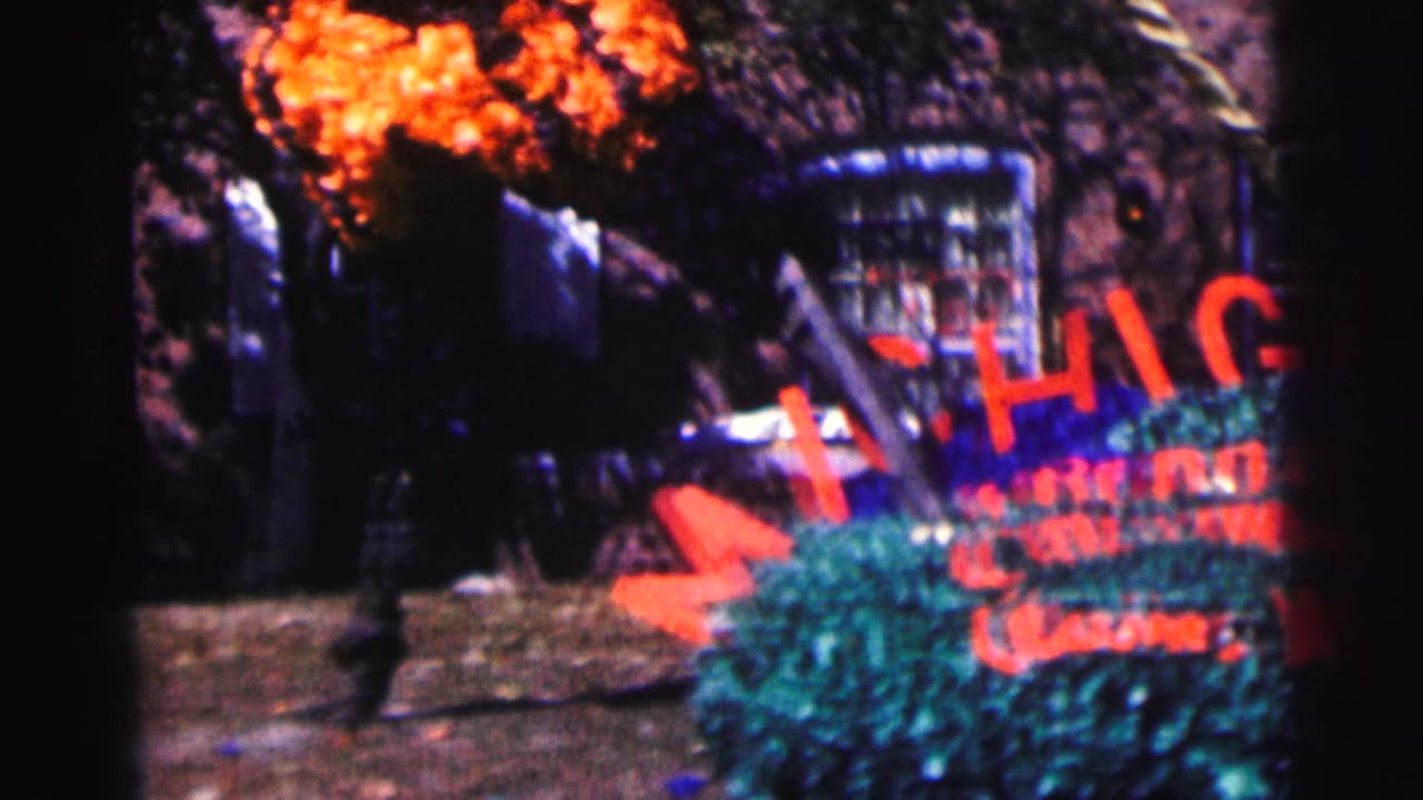 Garden display with red MICHIGAN letters partly blocked by foliage and tree shadow.