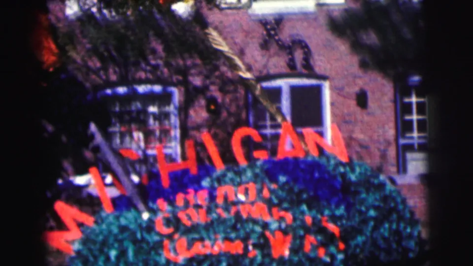 A closer 8mm view shows the MICHIGAN sign across greenery, smaller painted lettering below, and brick campus windows behind.