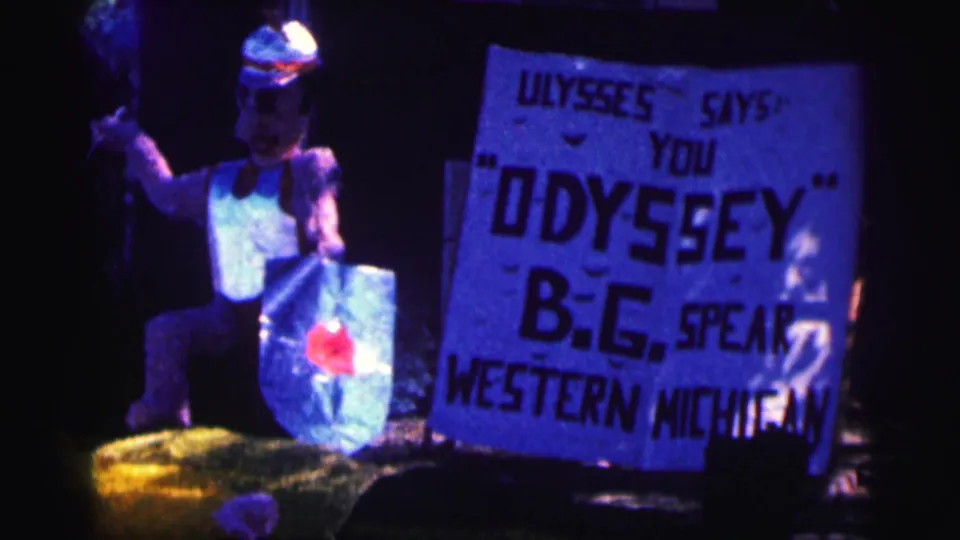 1963 Bowling Green University frame showing a large sign reading ULYSSES SAYS YOU ODYSSEY B.G. SPEAR WESTERN MICHIGAN beside a costumed figure.