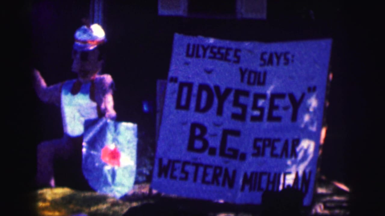 1963 Bowling Green University home-movie frame showing a costumed figure and a hand-painted sign referencing Ulysses, Odyssey, B.G., and Western Michigan.